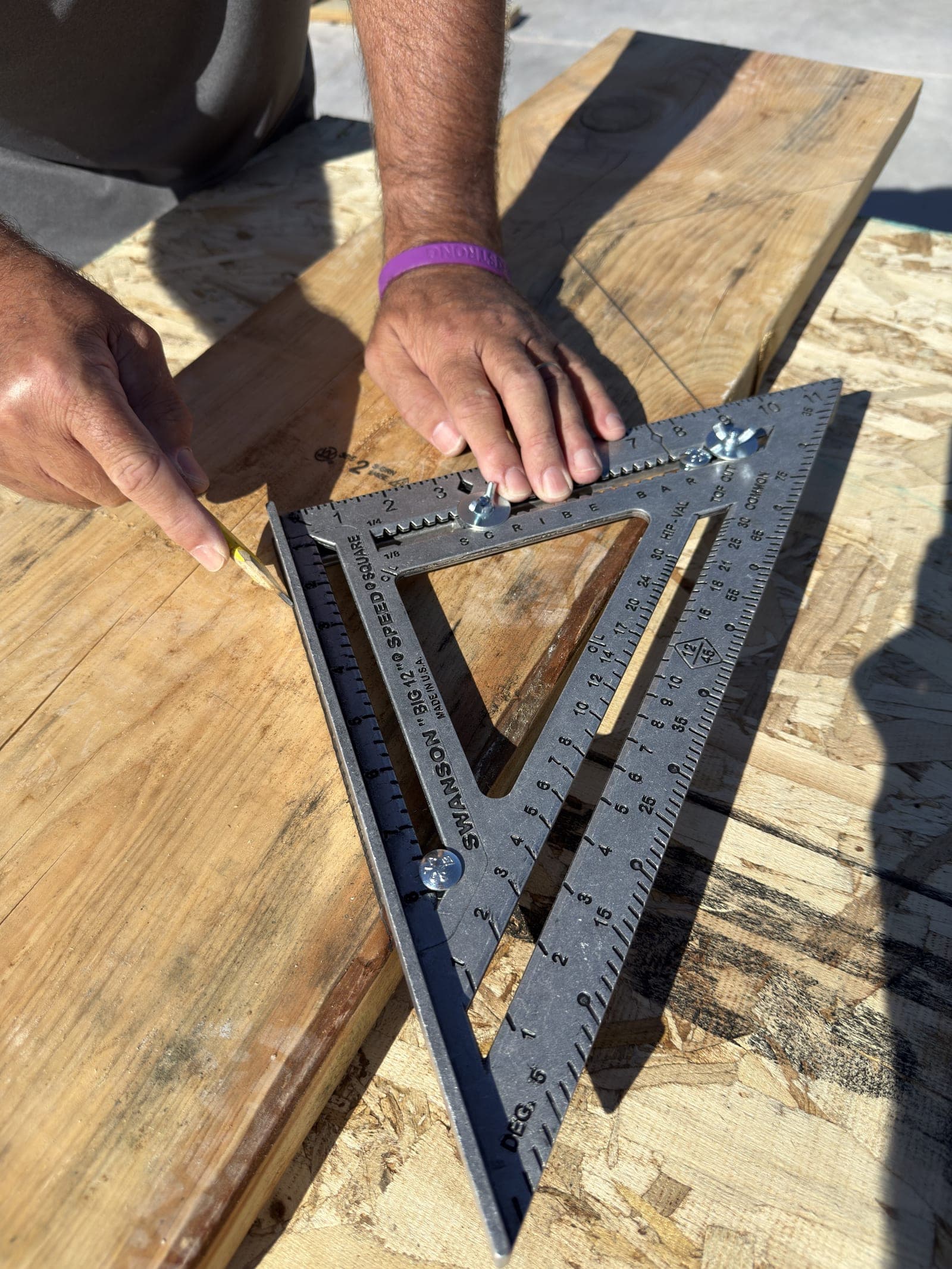 Hands using a Swanson Big 12 Speed® Square on framing lumber on a jobsite.